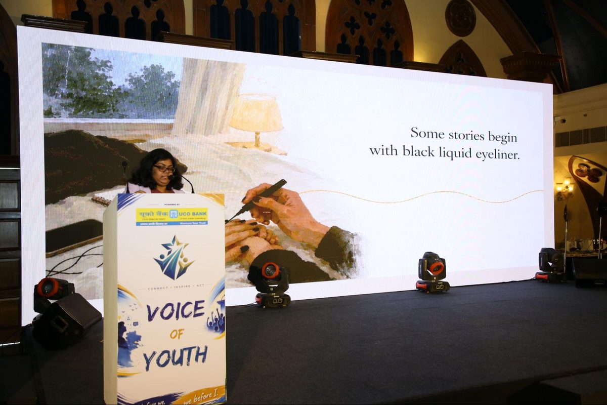 A Gen Uprising presenter at the podium beside a slide reading Some stories begin with black liquid eyeliner