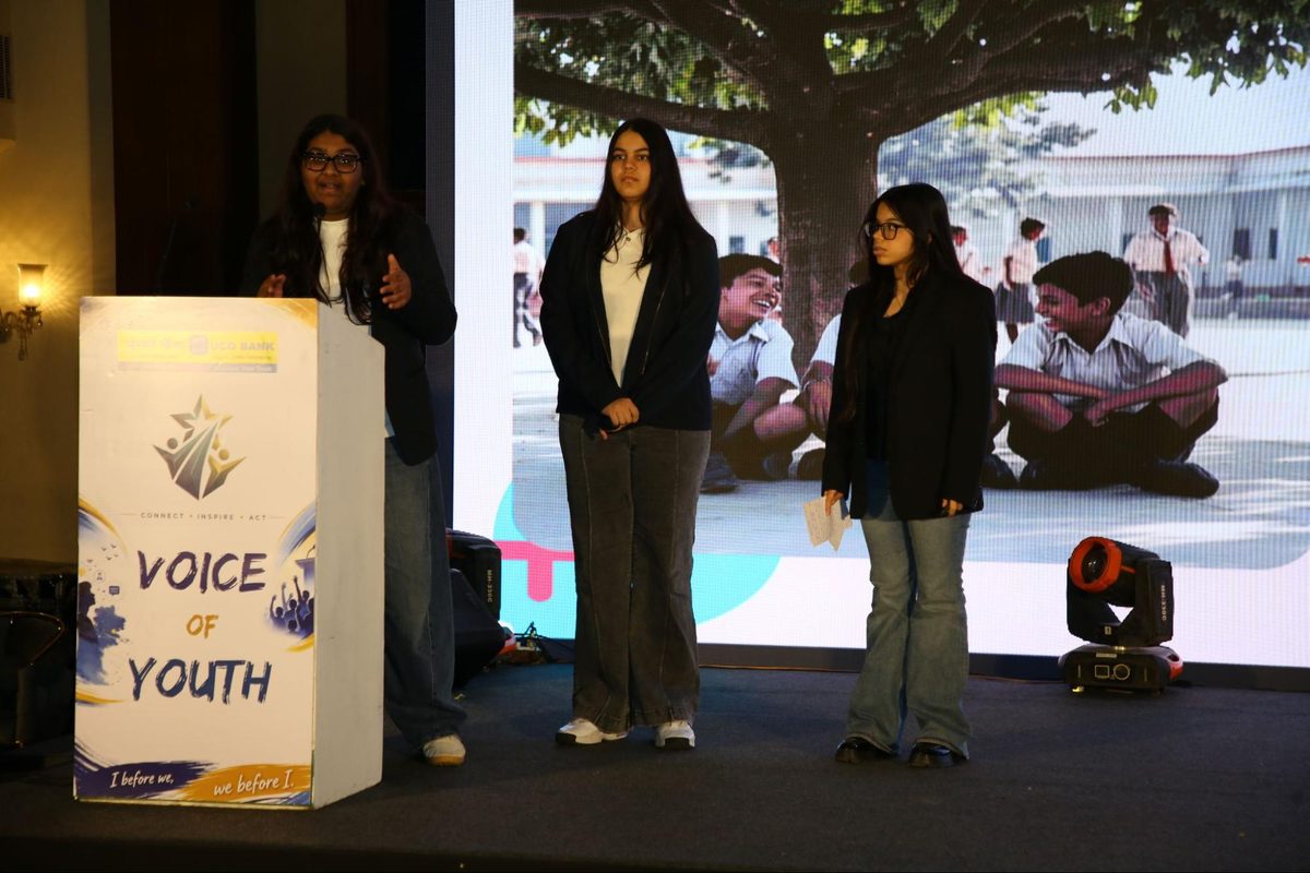 Ujjwal Bhavishya presenters on stage beside a slide of schoolchildren under a tree
